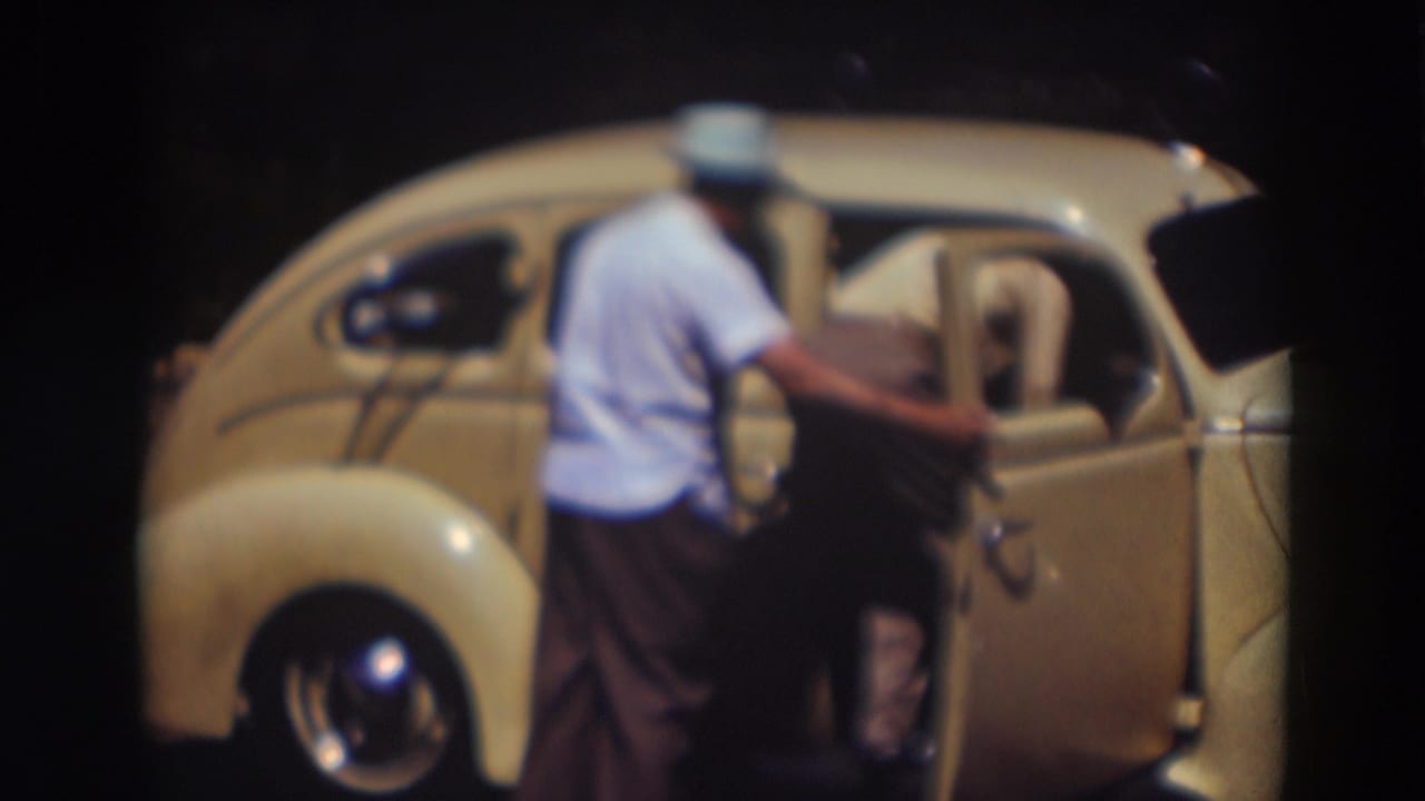 A man bends into the open side of the pale yellow compact car while another man waits behind him in the 1937 Truckee footage.