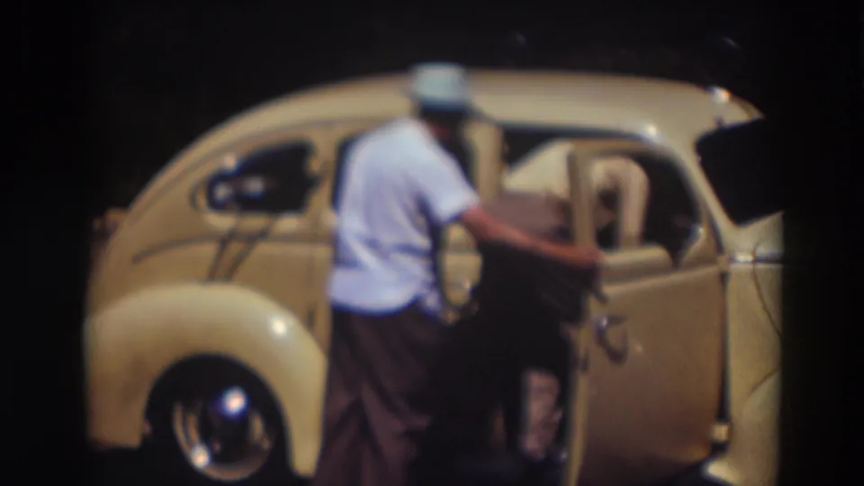 A man bends into the open side of the pale yellow compact car while another man waits behind him in the 1937 Truckee footage.
