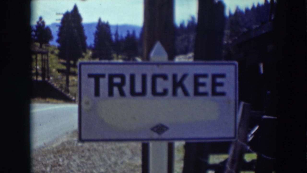 1937 8mm frame of a Truckee, California road sign near a quiet roadside with pines, distant hills, and soft film color.