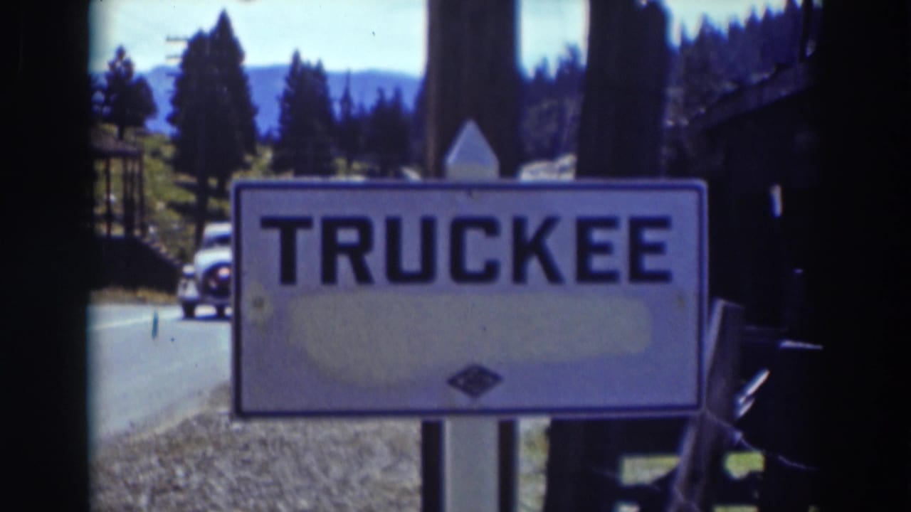 Truckee, California place sign fills the frame as a car passes behind it on a tree-lined road in 1937 home-movie footage.