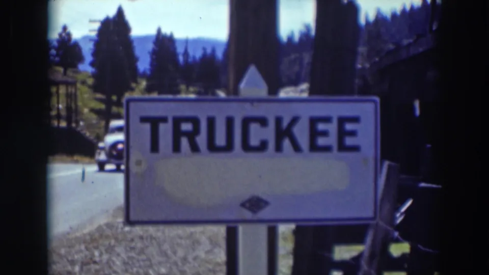 Truckee, California place sign fills the frame as a car passes behind it on a tree-lined road in 1937 home-movie footage.