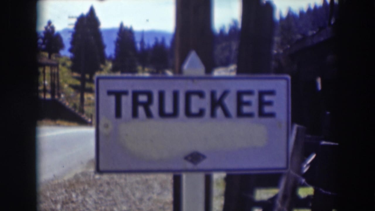 Soft 8mm view of the Truckee road sign set against a roadside, conifers, and distant mountain terrain in California.
