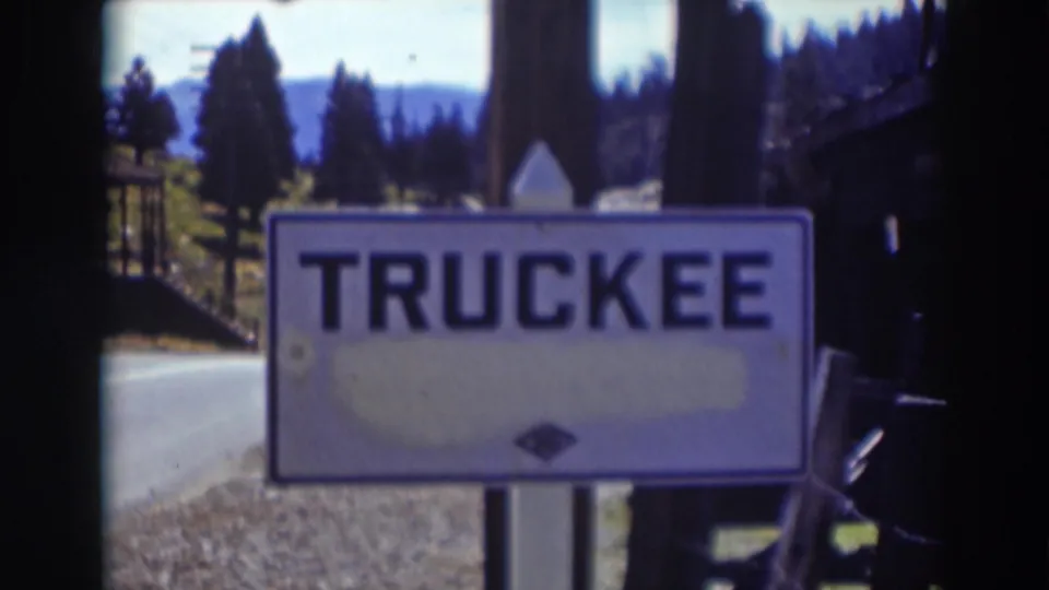 Soft 8mm view of the Truckee road sign set against a roadside, conifers, and distant mountain terrain in California.