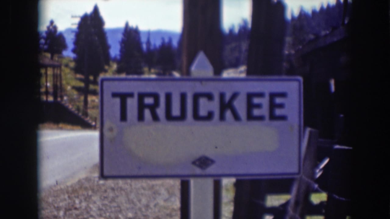 Final 1937 home-movie frame of the Truckee, California sign beside a rural road, framed by dark scan edges and pine-covered hills.