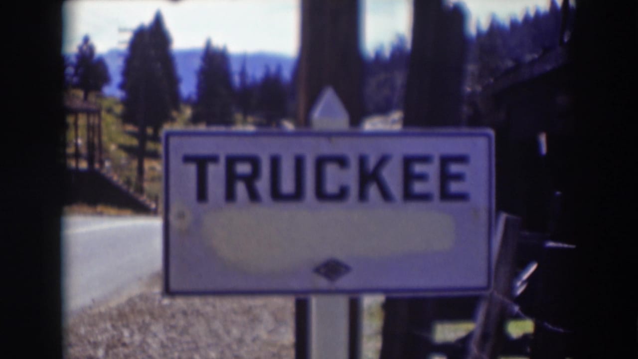 White TRUCKEE sign beside a road in Truckee, California, with pine trees and distant mountains in soft 1930s 8mm footage.