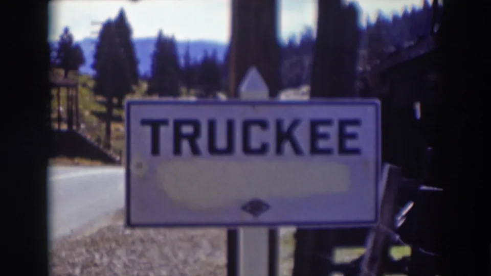 White TRUCKEE sign beside a road in Truckee, California, with pine trees and distant mountains in soft 1930s 8mm footage.
