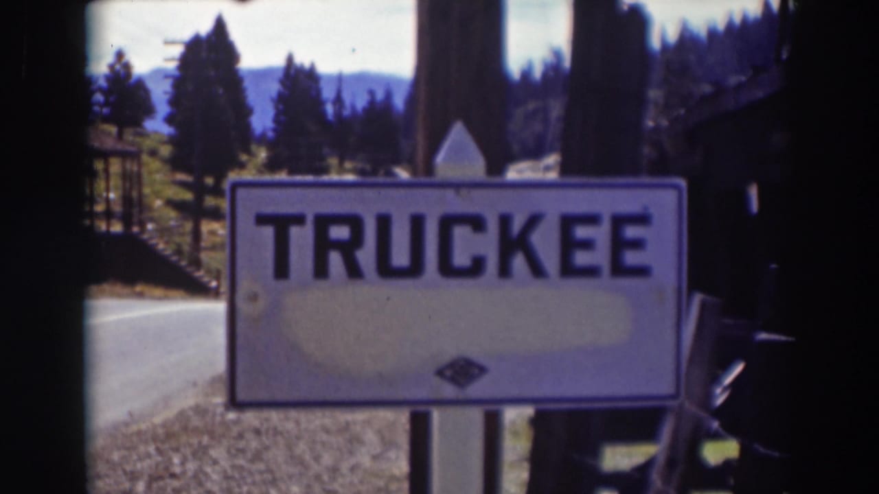 Truckee location sign fills the frame, with a road, evergreen trees, and mountains visible behind it in archival 8mm color.