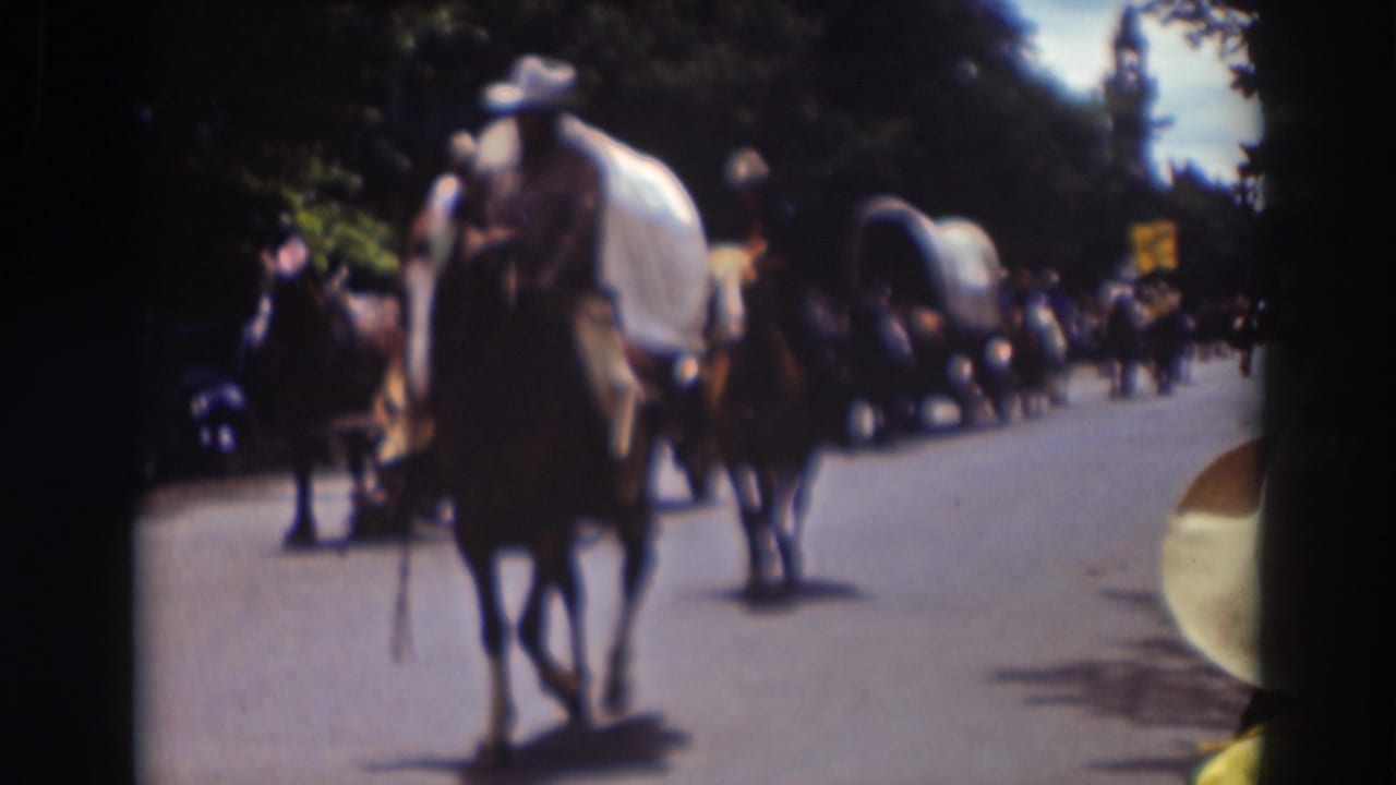 A horseback rider is centered in the 1937 Truckee parade view, with covered wagons, trees, spectators, and parked cars receding behind.