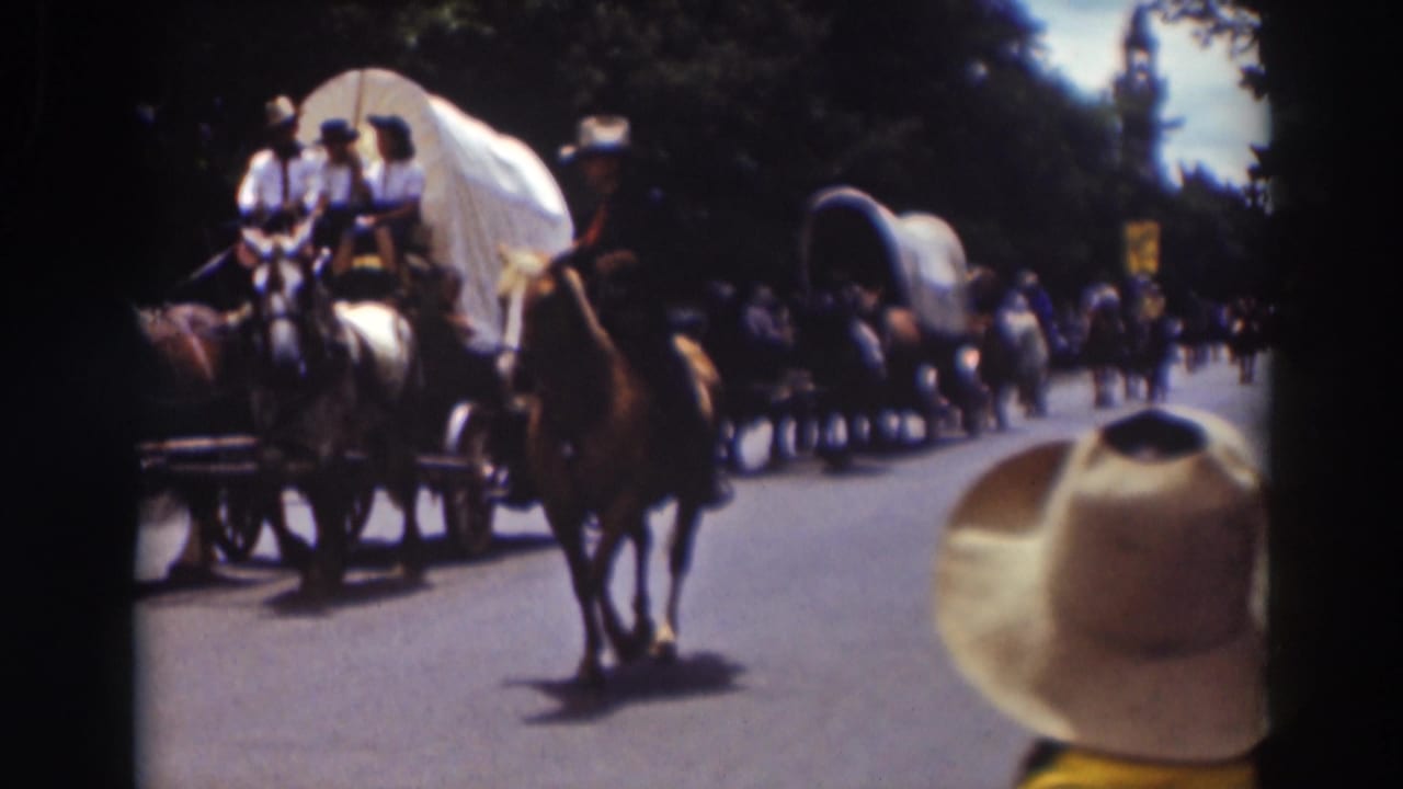 1937 Truckee parade frame showing a mounted rider, horse-drawn covered wagons, distant spectators, and a foreground cowboy hat.