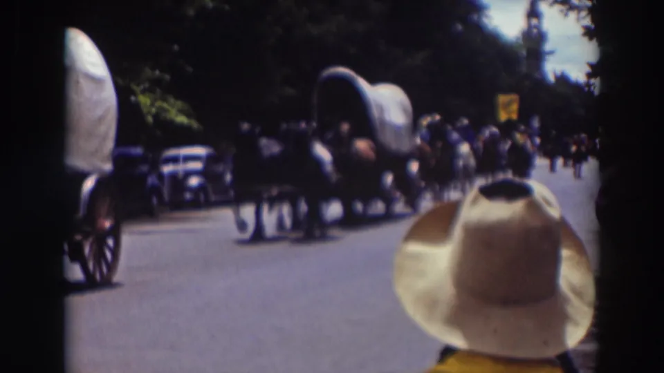 In supplied 1937 Truckee footage, a horse-drawn covered wagon moves along a tree-lined street before spectators and parked cars.