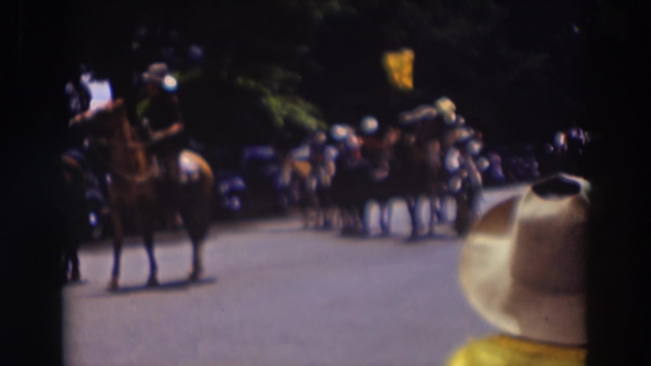 A rider on horseback appears in the Truckee parade scene, with spectators, vintage cars, trees, and a foreground hat in view.