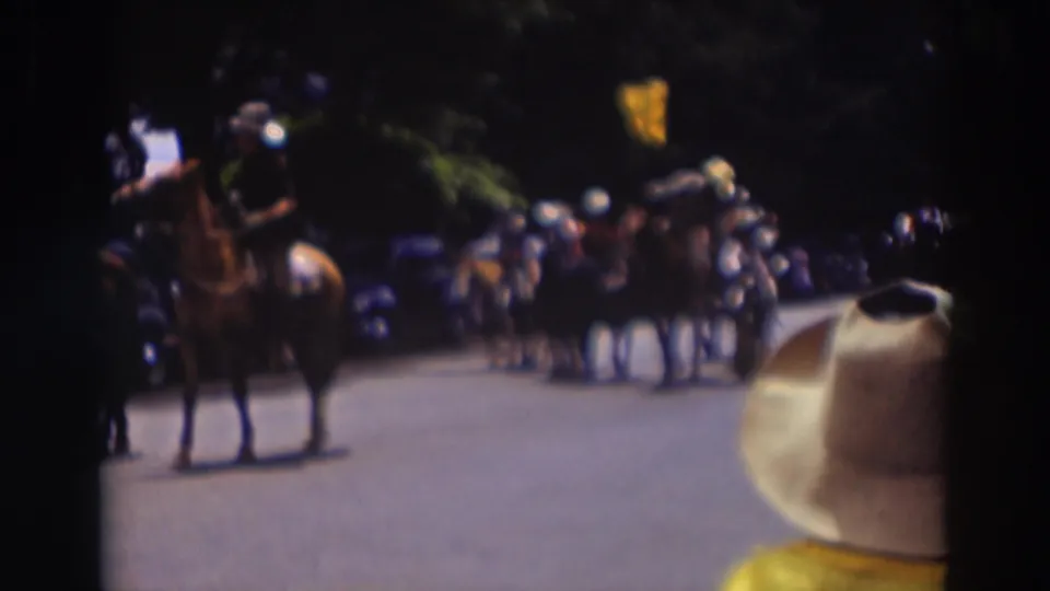 A rider on horseback appears in the Truckee parade scene, with spectators, vintage cars, trees, and a foreground hat in view.