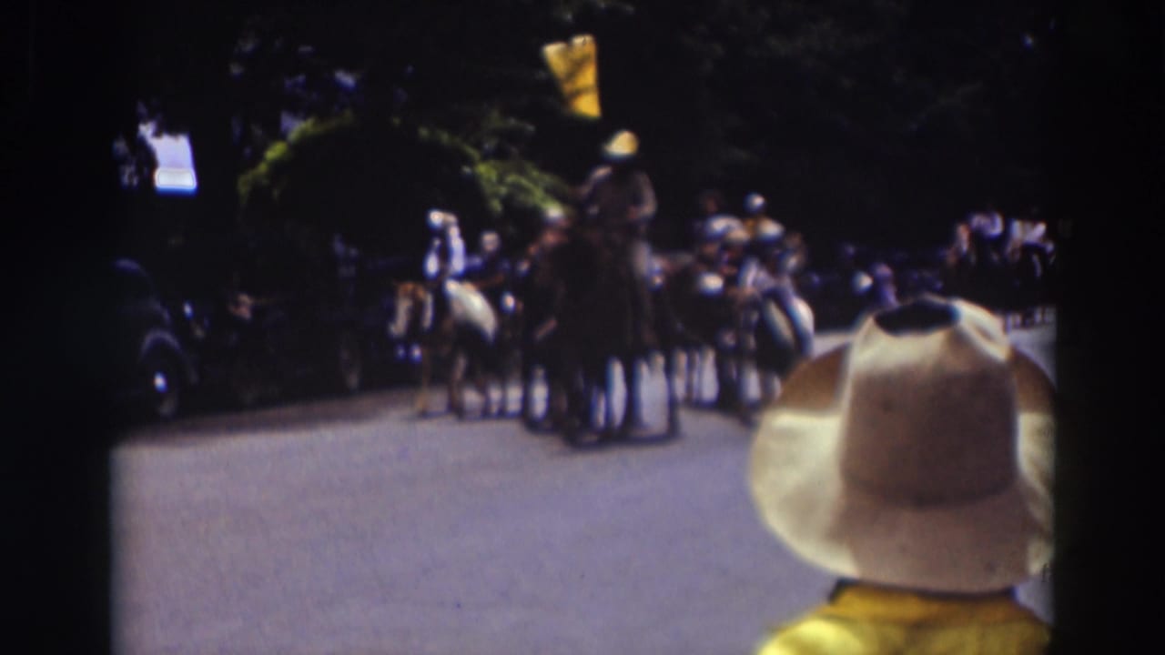 A home-movie view of the Truckee parade shows riders on horseback in the street, with a white cowboy hat filling the foreground.