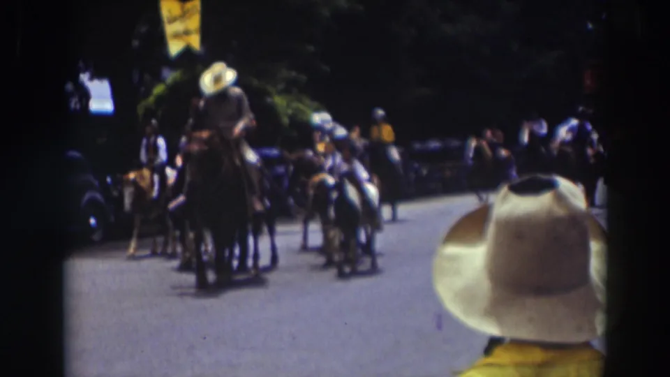 Horseback riders proceed through the Truckee parade while a spectator in a white cowboy hat remains in the foreground of the 8mm frame.