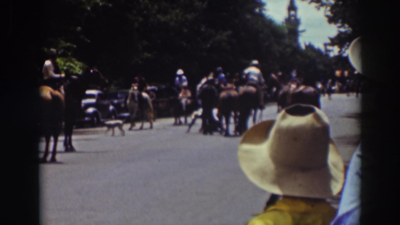 1937 Truckee 8mm frame showing riders on horseback gathered on a wooded road, viewed from behind a spectator in a light cowboy hat.