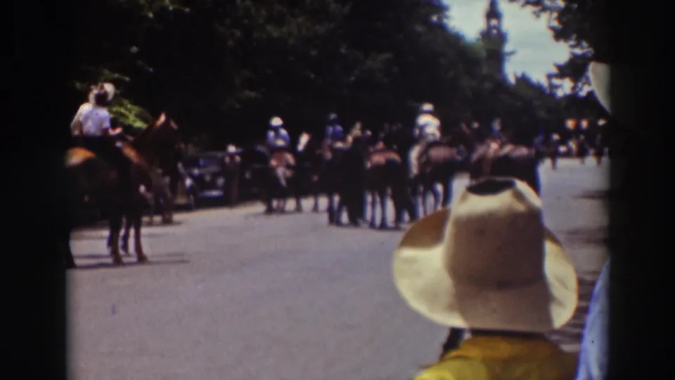 1937 Truckee home-movie frame with riders, horses, spectators, and parked automobiles along a shaded road.