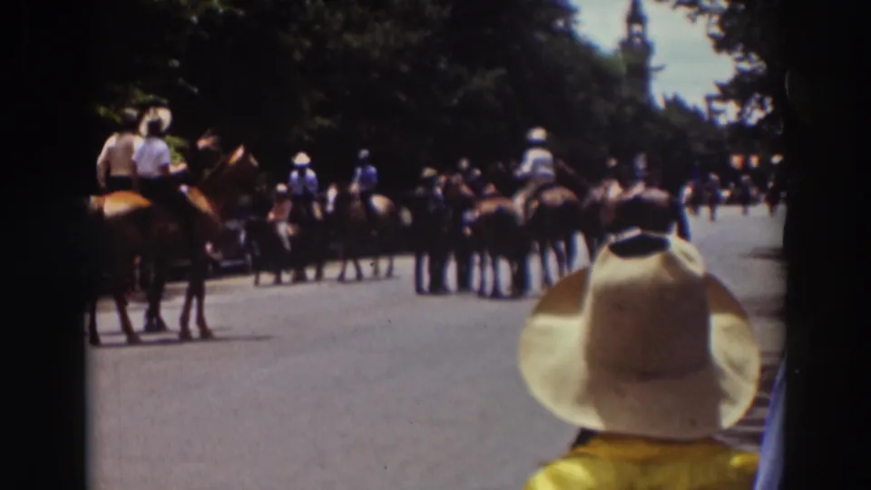 1937 Truckee 8mm frame showing horseback riders clustered on a road while a spectator in a cowboy hat watches from foreground.