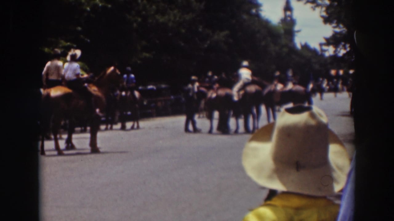 Late-1930s Truckee home-movie frame with horses, riders, spectators, and automobiles on a tree-lined road.