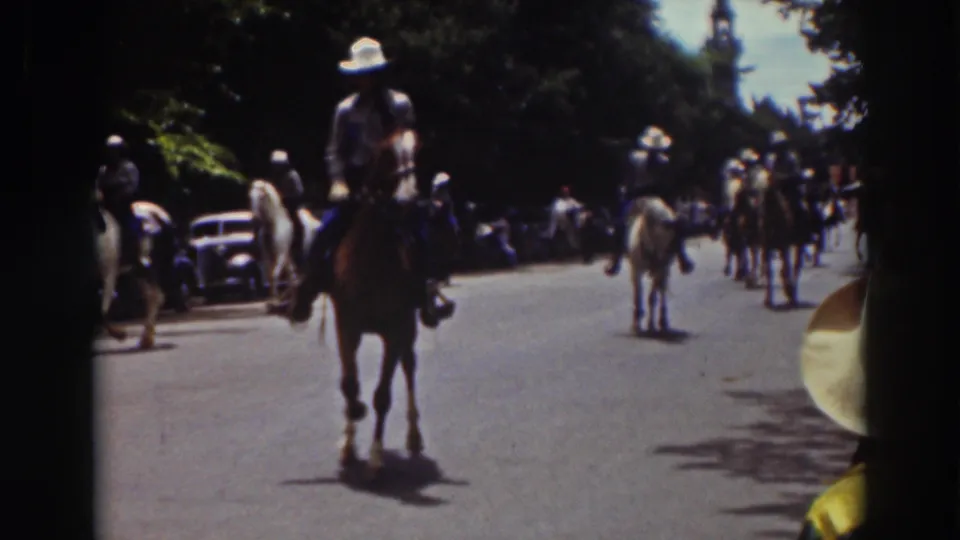 1937 Truckee parade frame showing a rider on horseback near the camera, with more mounted riders and spectators down the street.