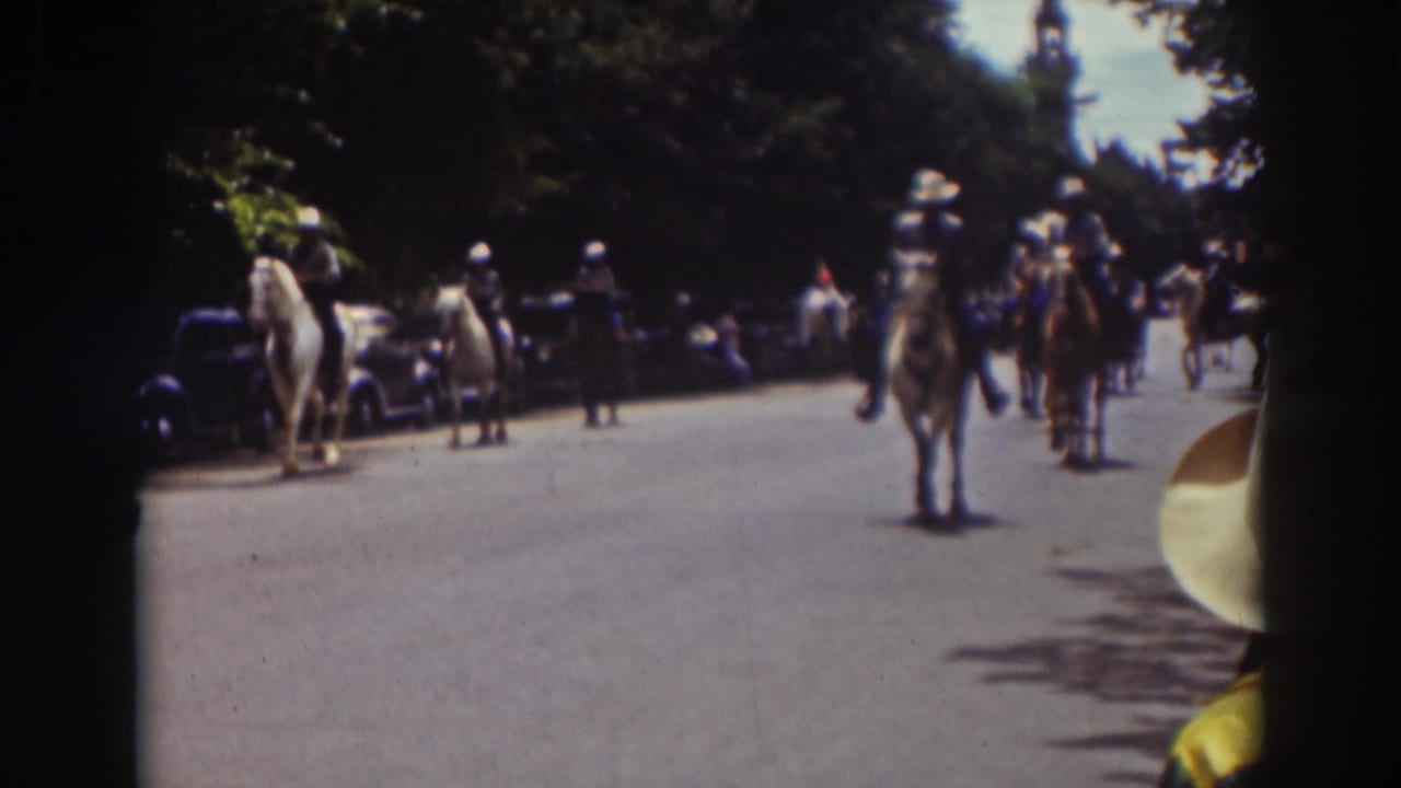 Mounted riders in light hats continue along a Truckee street, with vintage cars and onlookers visible beside the route.