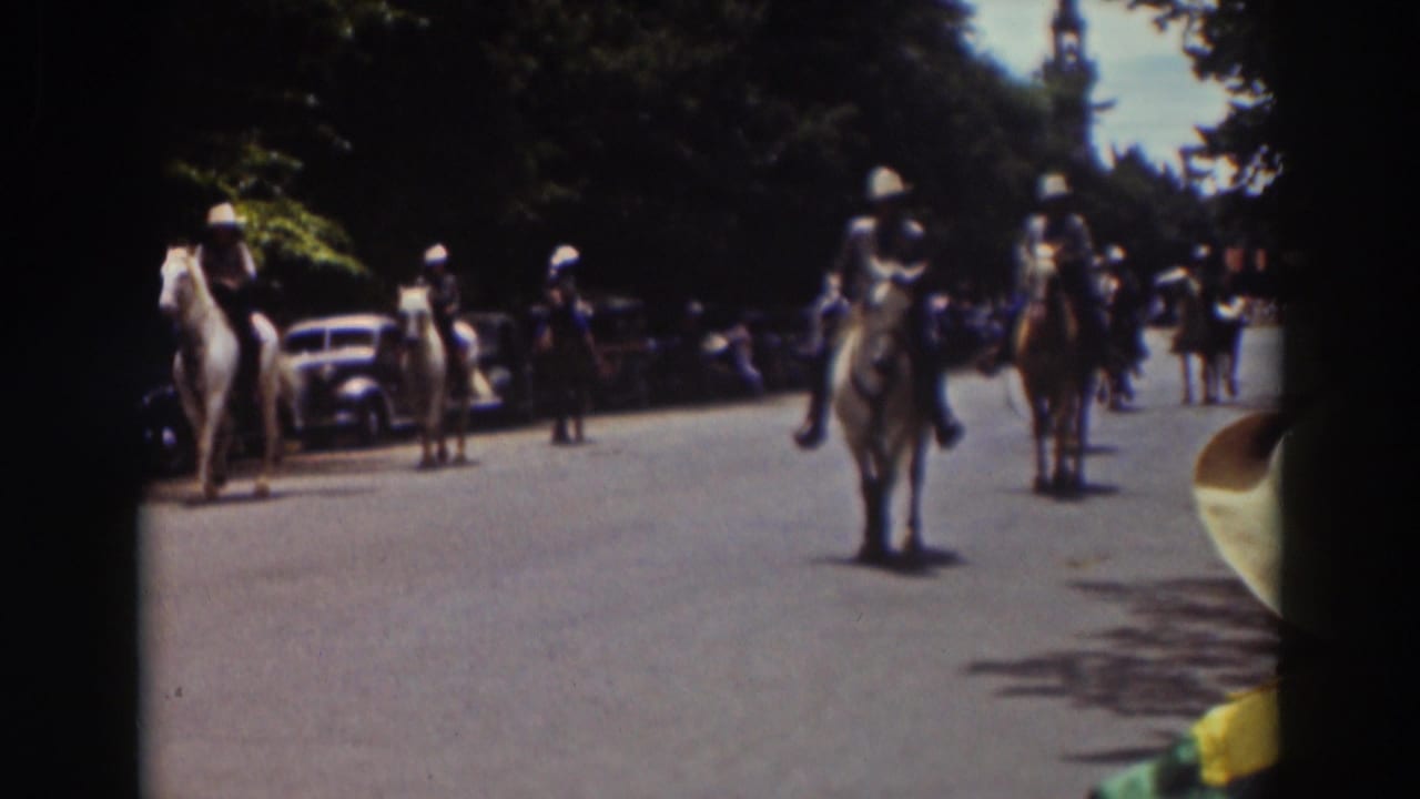 A roadside 8mm view shows mounted parade participants approaching on a wide Truckee street lined with cars and trees.