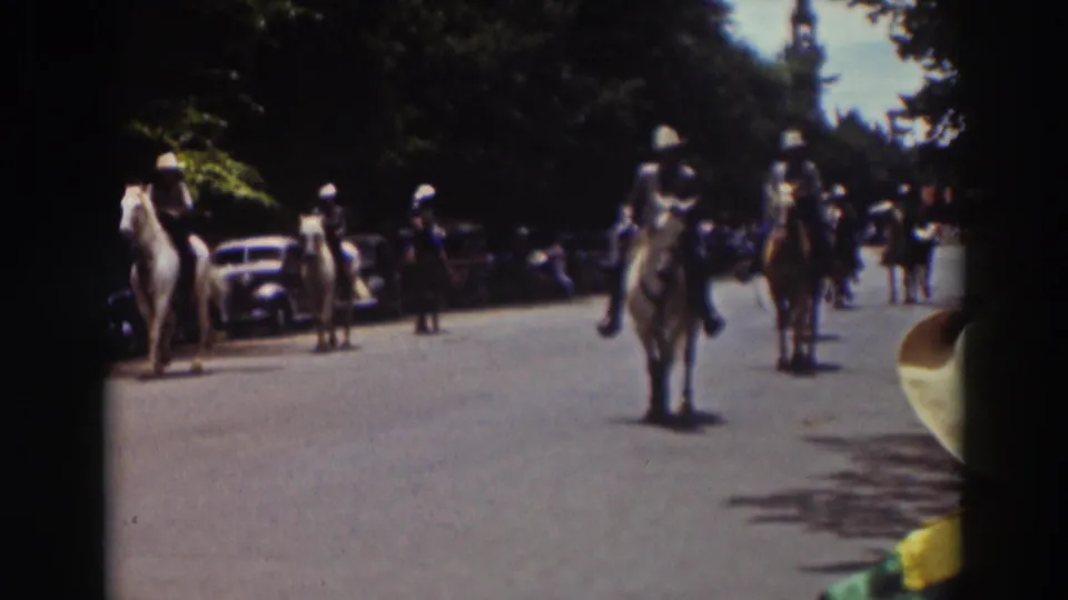 A roadside 8mm view shows mounted parade participants approaching on a wide Truckee street lined with cars and trees.