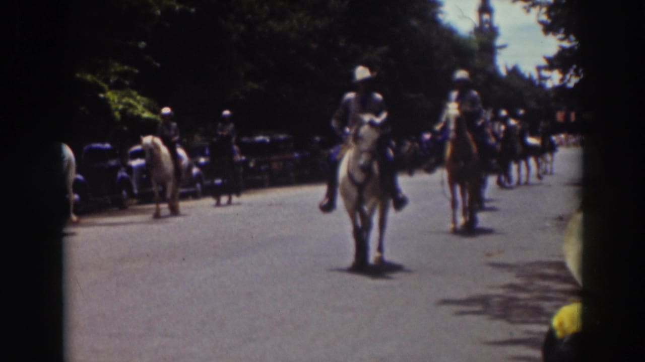 Late frame of the Truckee mounted procession, with two riders prominent and additional horses, cars, and spectators behind them.