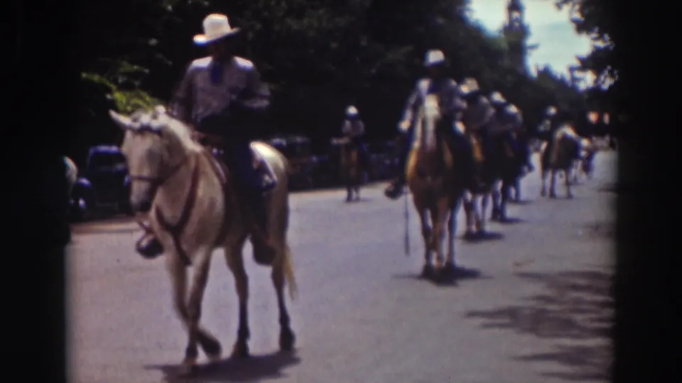 In the Truckee parade scene, a mounted rider passes near the camera as additional riders continue down the sunlit street.