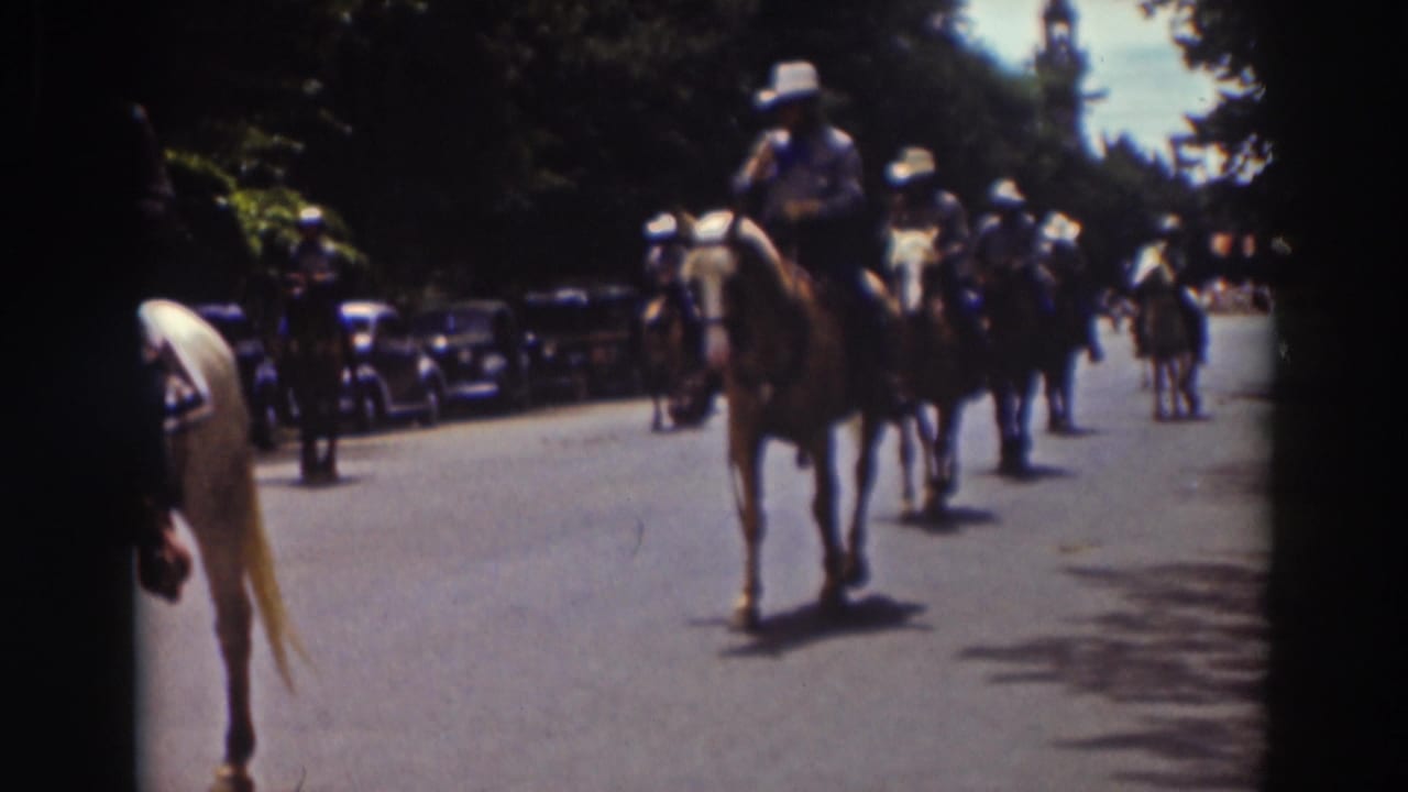 A mounted rider on a darker horse advances in the 1937 Truckee parade, with another horse partly cropped at the left edge and cars along the street.