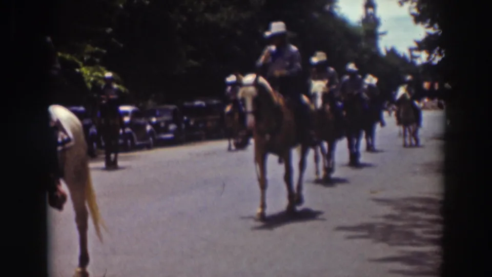 A mounted rider on a darker horse advances in the 1937 Truckee parade, with another horse partly cropped at the left edge and cars along the street.