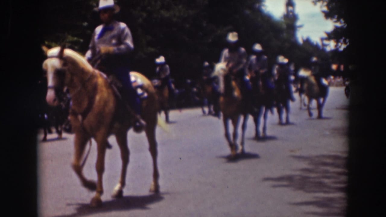 A rider on a light-colored horse passes close to the camera with more riders behind.