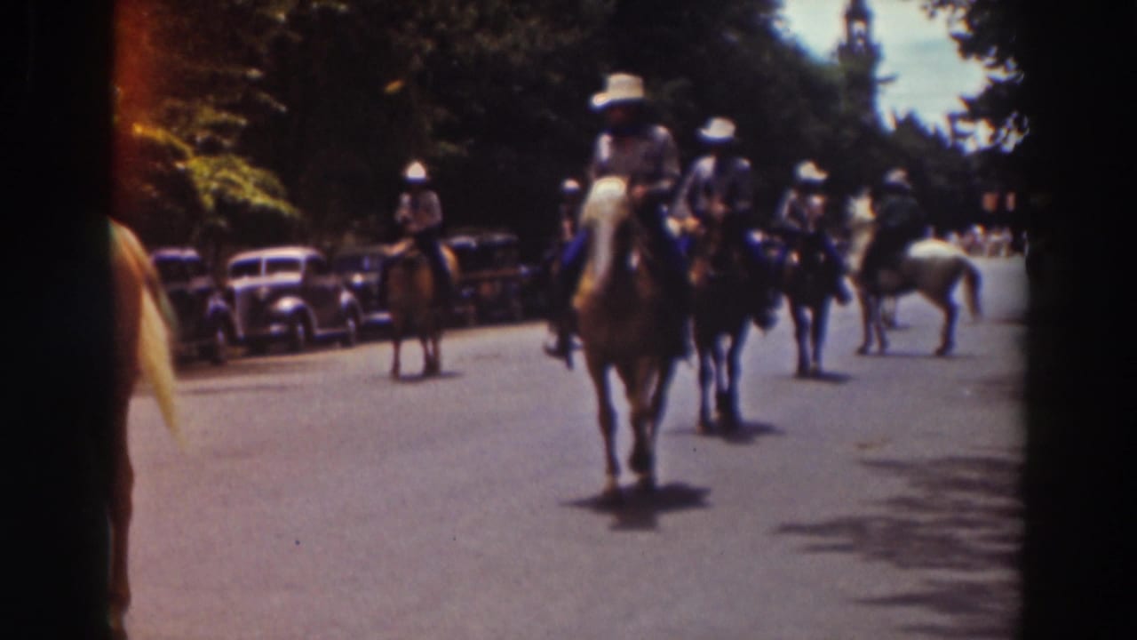 Mounted parade participants approach the camera in the Truckee street scene, with rounded 1930s-era automobiles visible along the curb.