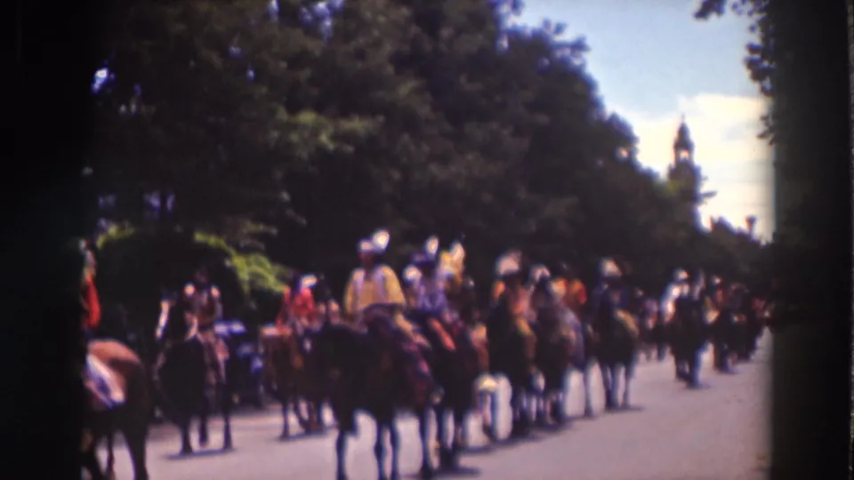 Costumed riders continue through Truckee, California, in a horseback parade, with trees and a distant steeple visible behind them.