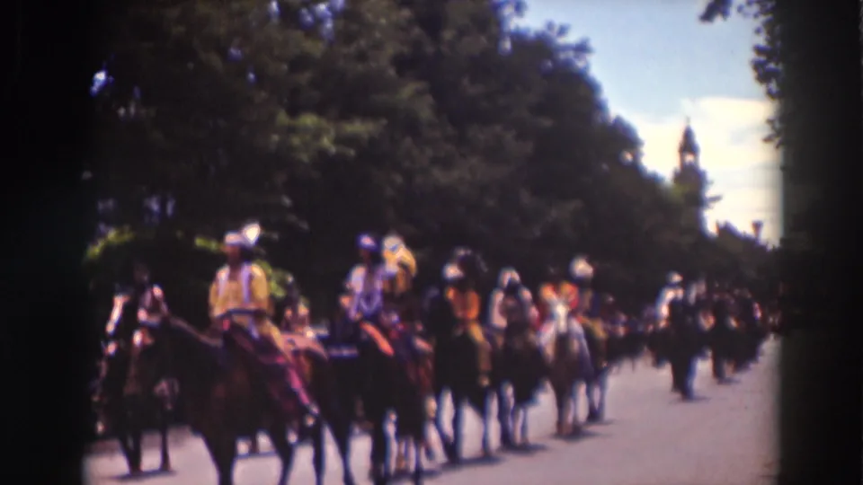 A closer 1937 Truckee frame shows several costumed horseback riders in formation on a sunlit street lined with trees.