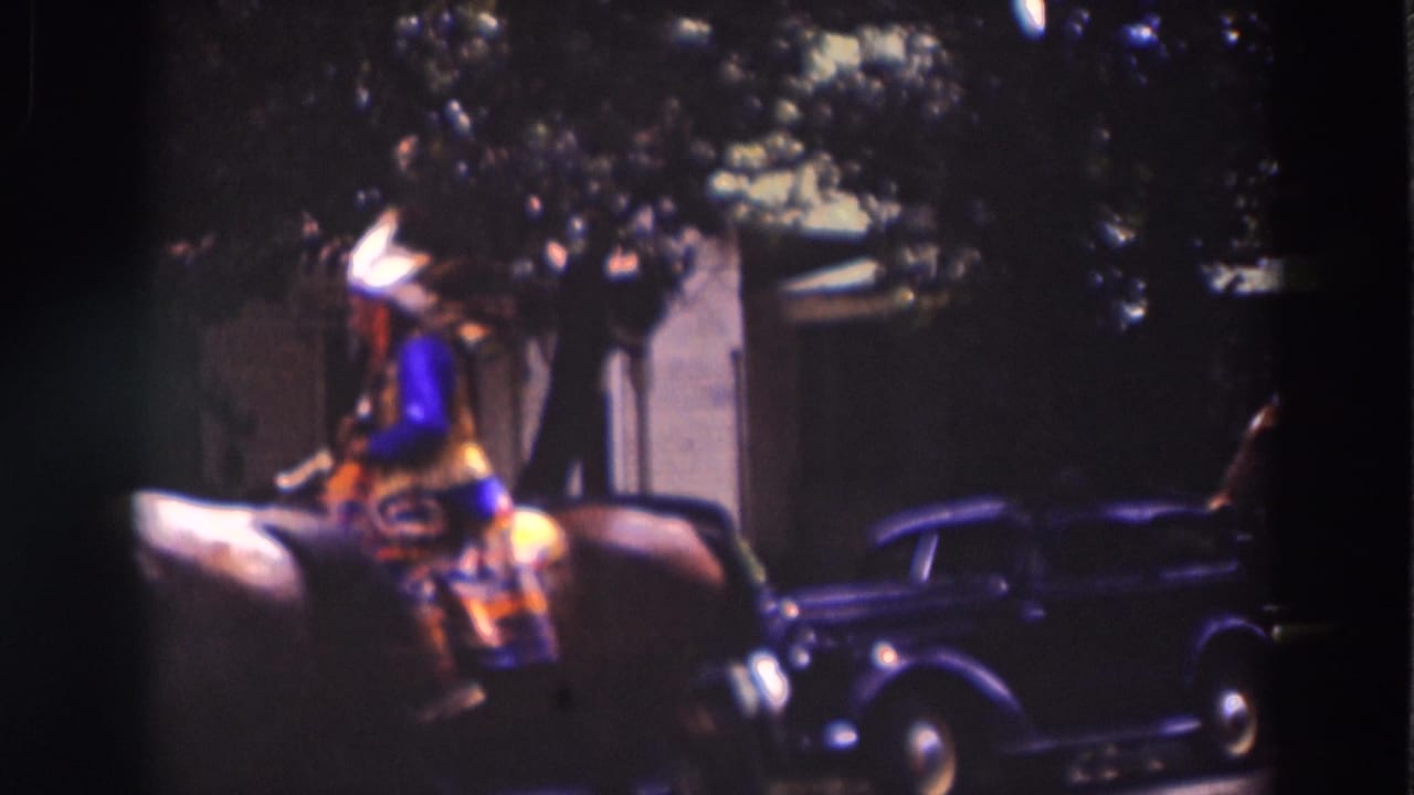 A horseback rider in Native American-inspired parade dress moves past a dark 1930s automobile under trees in Truckee.