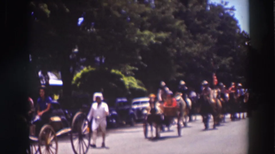 1937 Truckee parade scene with horse-drawn buggies, riders, pedestrians, and vintage cars along a sunny tree-lined street.