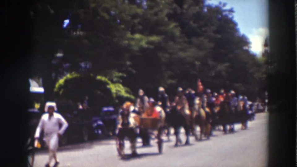 Horse-drawn buggies and mounted riders proceed through Truckee, California, with trees and parked cars visible along the road.