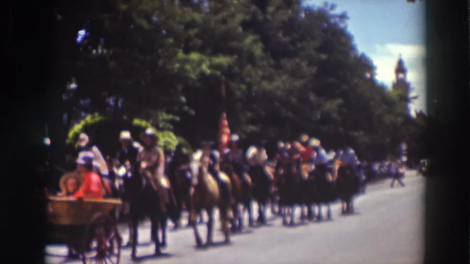 Mounted parade riders proceed behind a carriage on a tree-lined Truckee street, with spectators and flags visible.