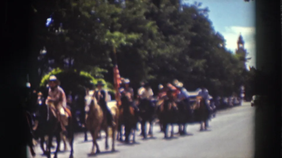 Truckee parade riders move past the camera in 1937 home-movie footage, with horses, flags, trees, and spectators in view.