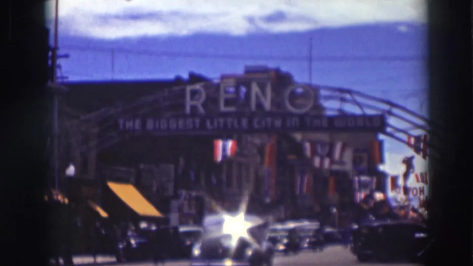 1937 street view with automobile headlight glare, storefronts, bunting, and the Reno arch visible above traffic.