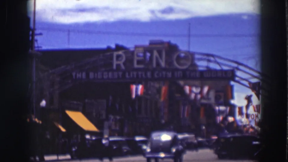 Soft 8mm frame of 1937 street traffic and pedestrians beneath the Reno arch, with awnings and bunting along the block.