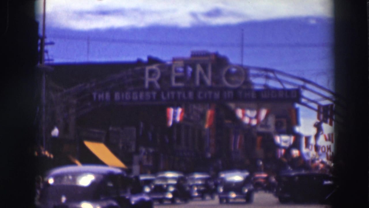 Reno arch sign above a busy street with cars, flags, and blue sky.