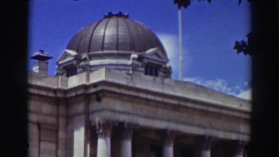 1937 Truckee home-movie frame centered on the dome and upper facade of the government building, with tree leaves at the edge.