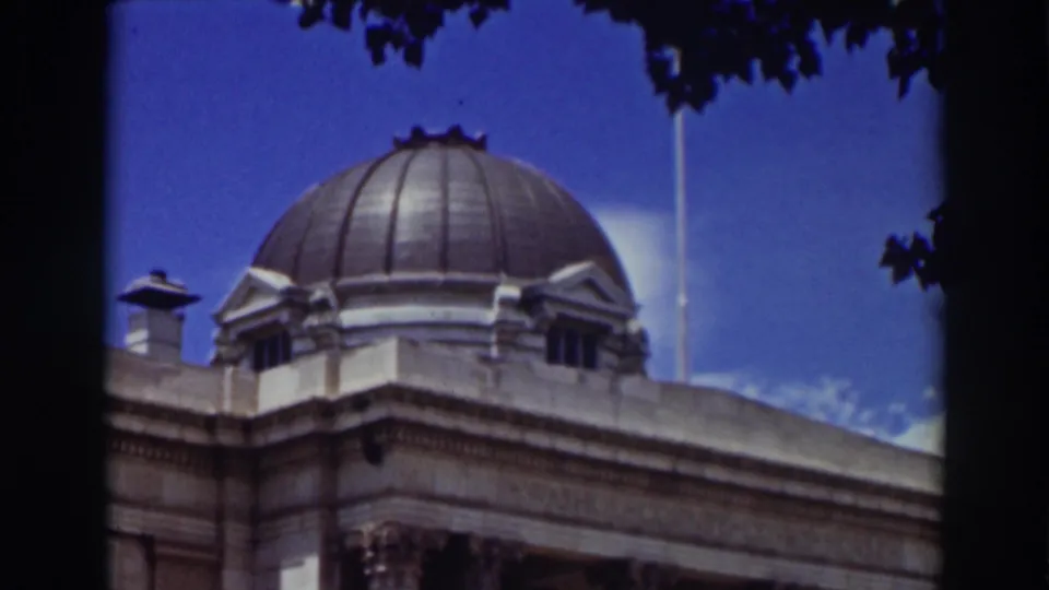 Late-frame 1937 Truckee view of the government building dome, roofline, and stone facade, partly bordered by dark tree branches.