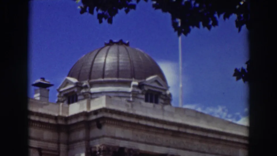 1937 Truckee home-movie frame showing a domed stone building with cornice detail beneath a blue sky and tree canopy.