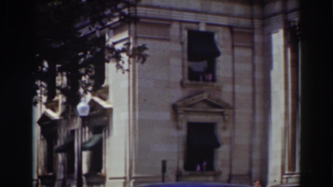 1937 Truckee home-movie frame showing lower stone facade details, dark awnings, shaded trees, and a lamppost near the building.