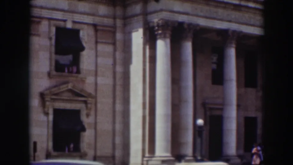 1937 Truckee frame showing a domed classical building with tall columns, stonework, dark awnings, and blue sky.