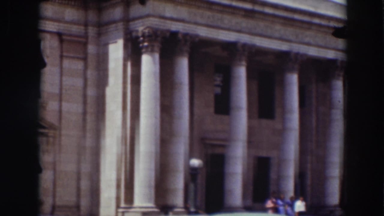 Columned courthouse facade with entrance, lamps, and a few people near the steps.