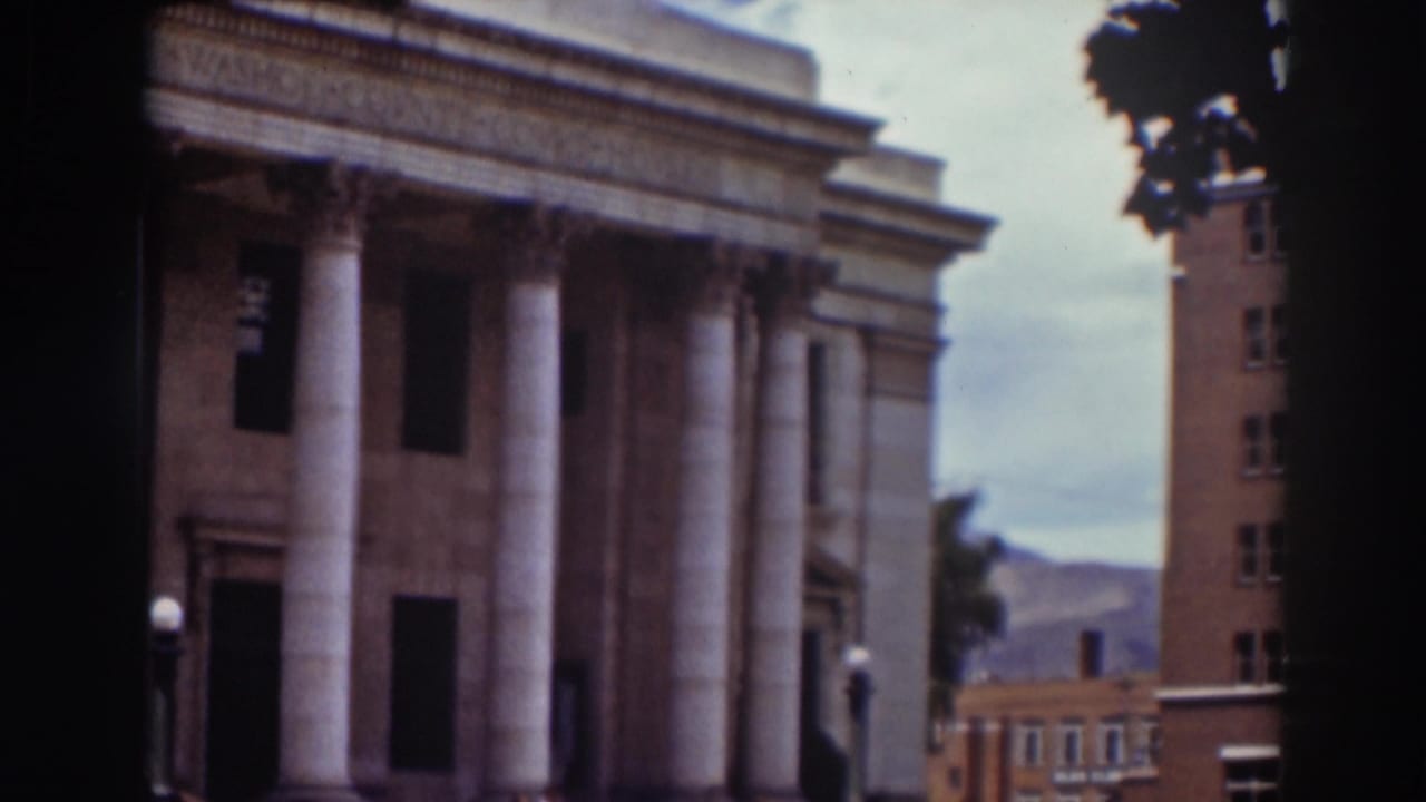 The camera shifts across the courthouse front, showing columns, a neighboring brick building, distant hills, and soft 8mm color.