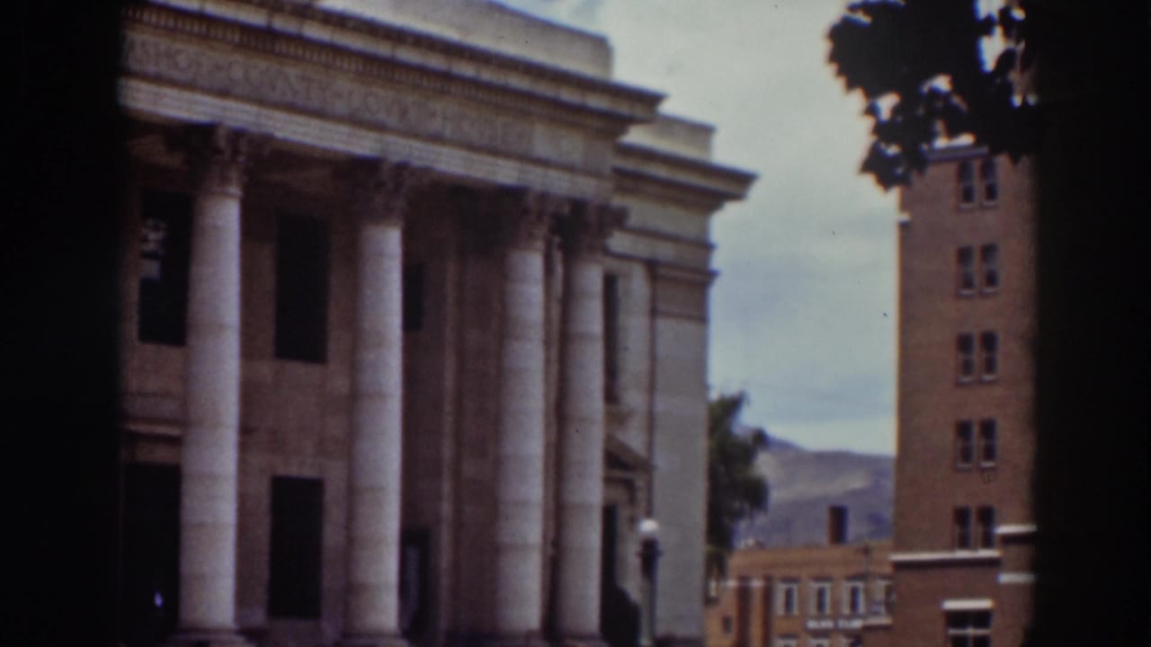Columned building beside a brick structure with hills in the distance.